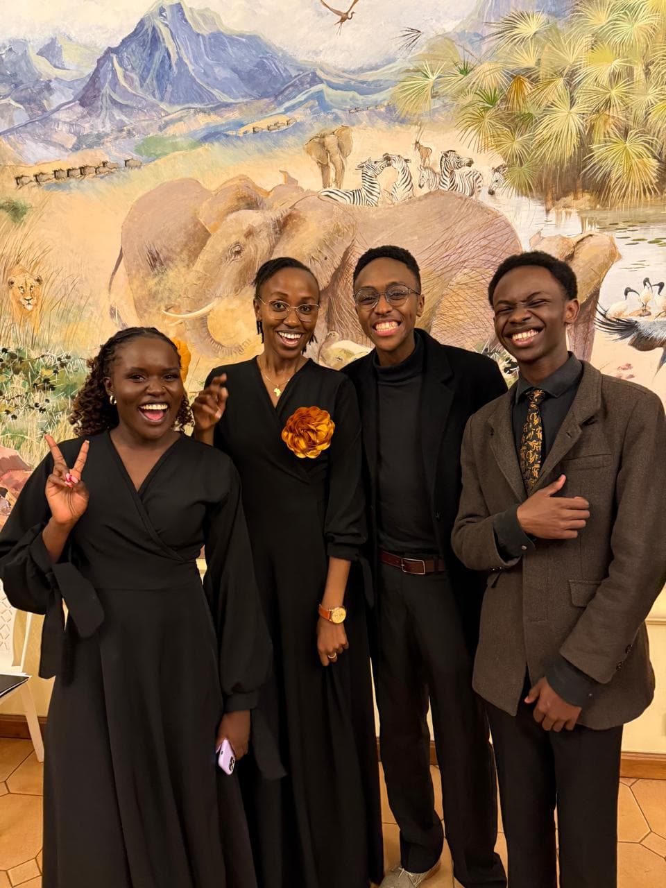 Four choristers in concert black before a painted Kenyan landscape mural